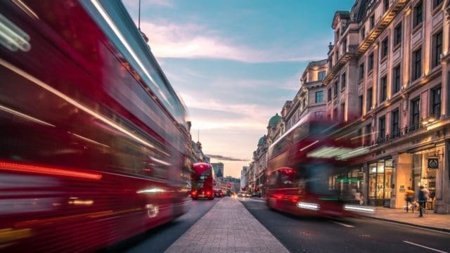 Blurry photo of red buses driving down a London street.