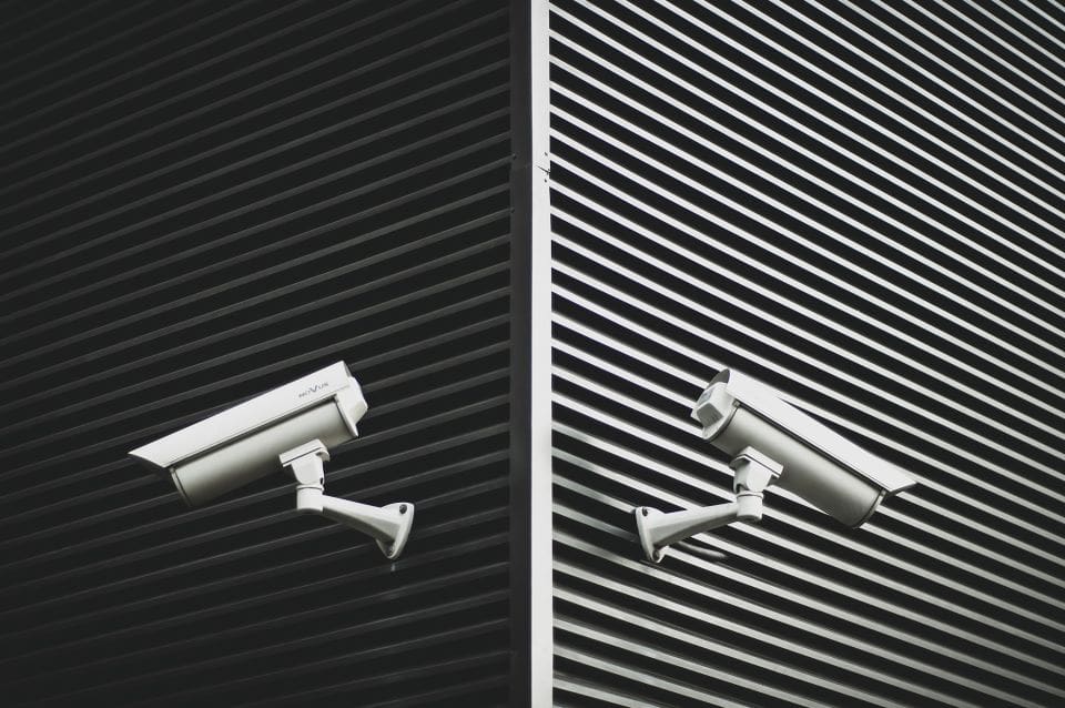 Two security cameras facing opposite directions on the corner of a building.