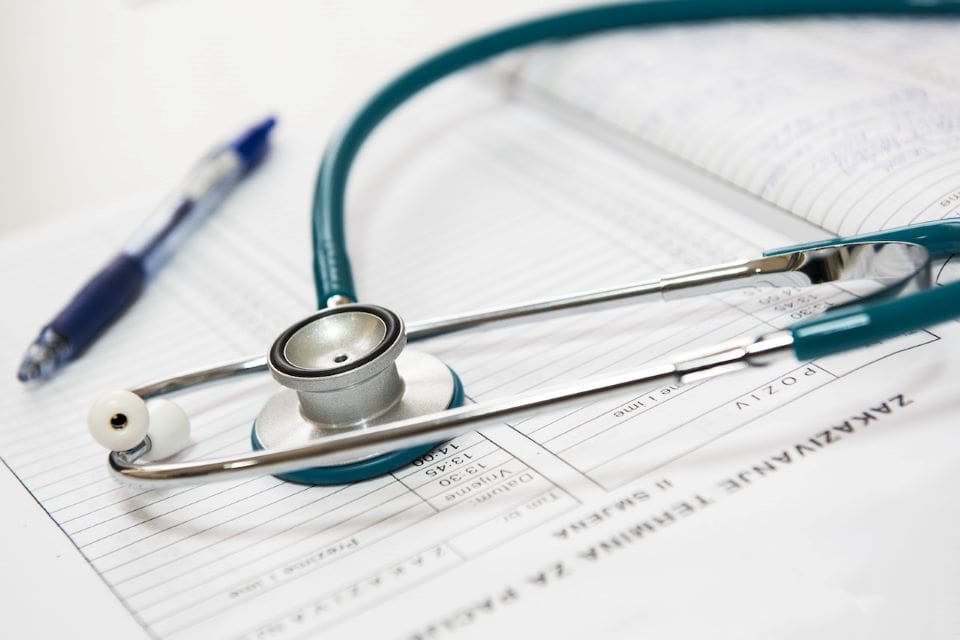 Blue and silver stethoscope laying on a medical chart next to a blue pen.