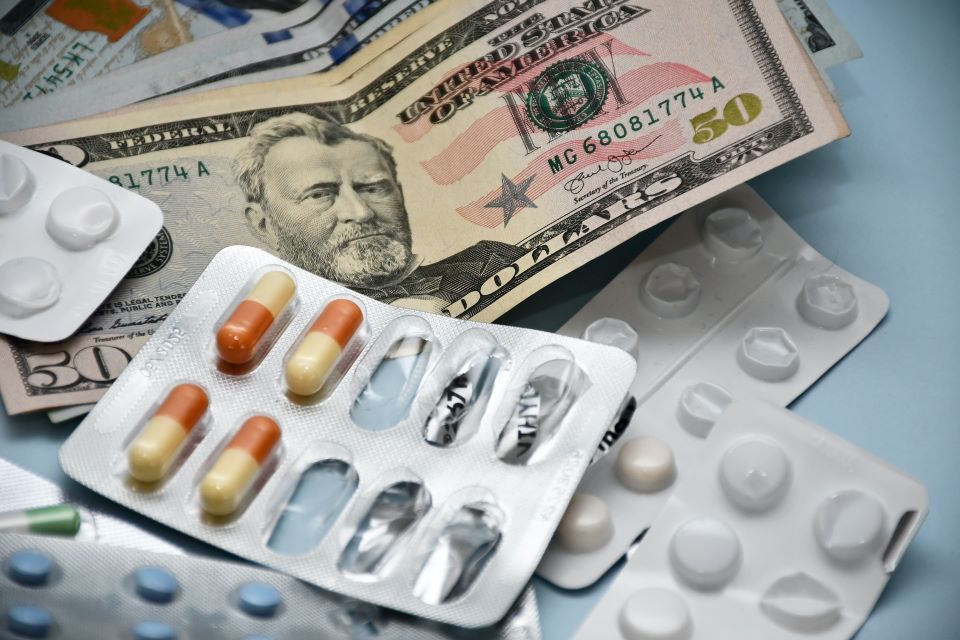 Assortment of pills in blister packs laying on a table with American dollar bills to demonstrate the alleged importance of money over medicine in the Cigna lawsuit.
