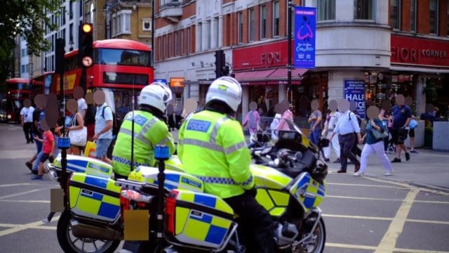 Two police officers on motor cycles watching people use a cross walk in the UK.